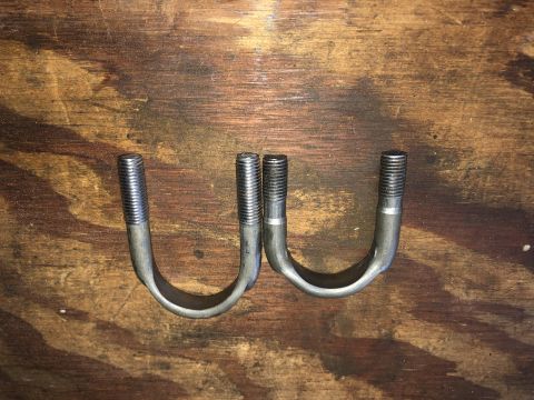1980 Ford Bronco - Two U-bolts are laid out on a weathered wooden surface. The U-bolts are made of metal and have threaded ends.