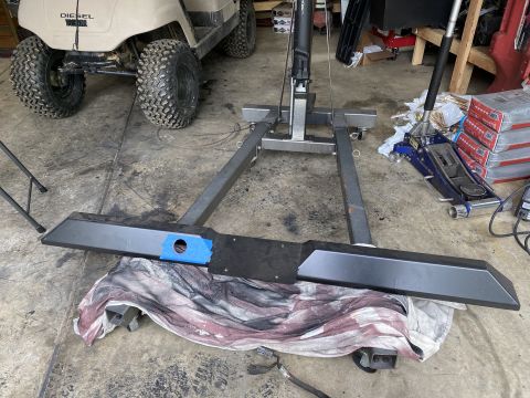 1994 Ford Bronco - An aftermarket rear bumper is laid out on a cloth, with an engine hoist positioned behind it. A golf cart is visible in the background.