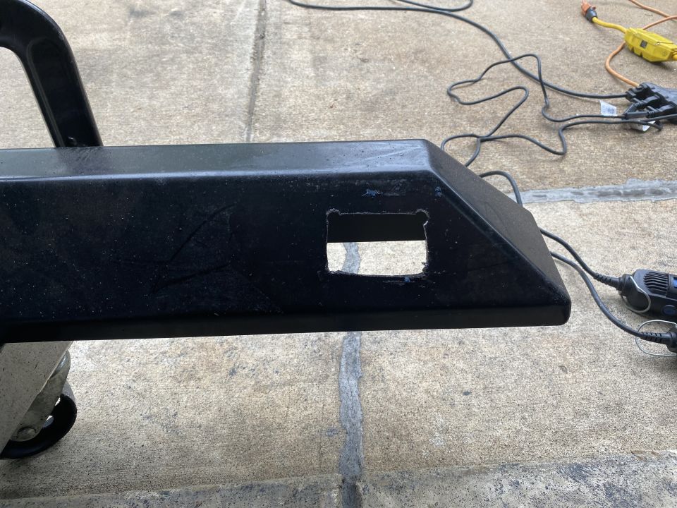 Black bumper with rectangular cutouts, resting on a dolly, with tools and cords nearby