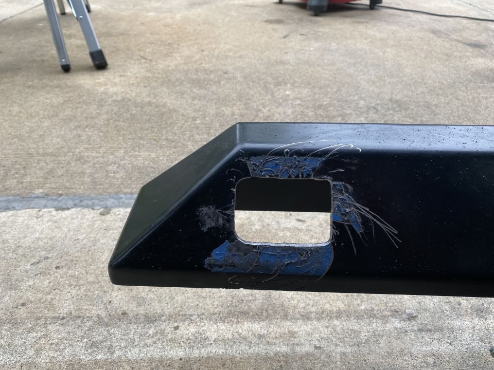 Black bumper part with a rectangular cut-out hole and visible damage