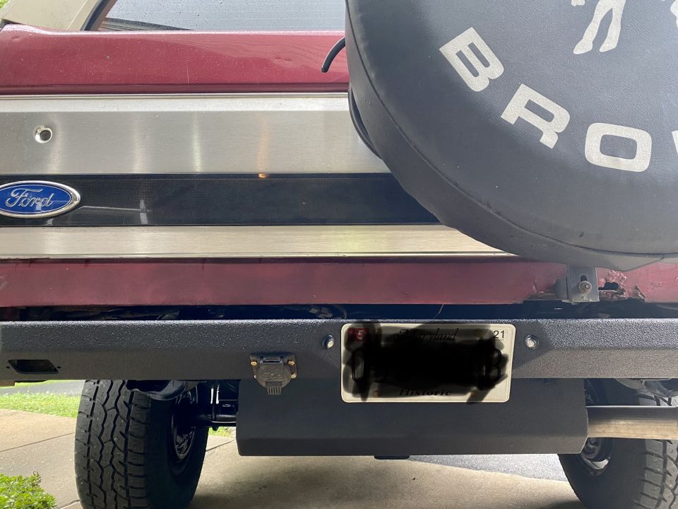 Rear view of a Ford Bronco with a spare tire cover that says BRONCO. Has a aftermarket bumper and license plate