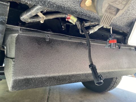 1994 Ford Bronco - Close-up of the underbody reveals a textured black box and wiring harness, with a partial Ford logo visible.