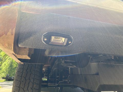 1994 Ford Bronco - An aftermarket LED light is installed on the textured rear bumper of a vehicle, with a tire and suspension components visible.