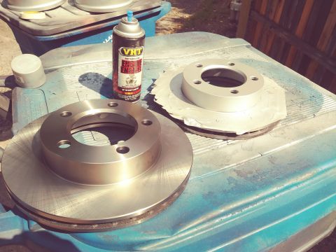 1996 Ford Bronco - Brake rotors and spray paint are laid out on a blue surface, suggesting preparation for a vehicle maintenance task.