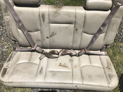 1980 Ford Bronco - This tan leather rear car seat, complete with seatbelts, displays significant staining and wear.