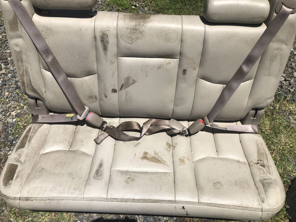 Tan leather rear car seat with seatbelts, showing stains and wear