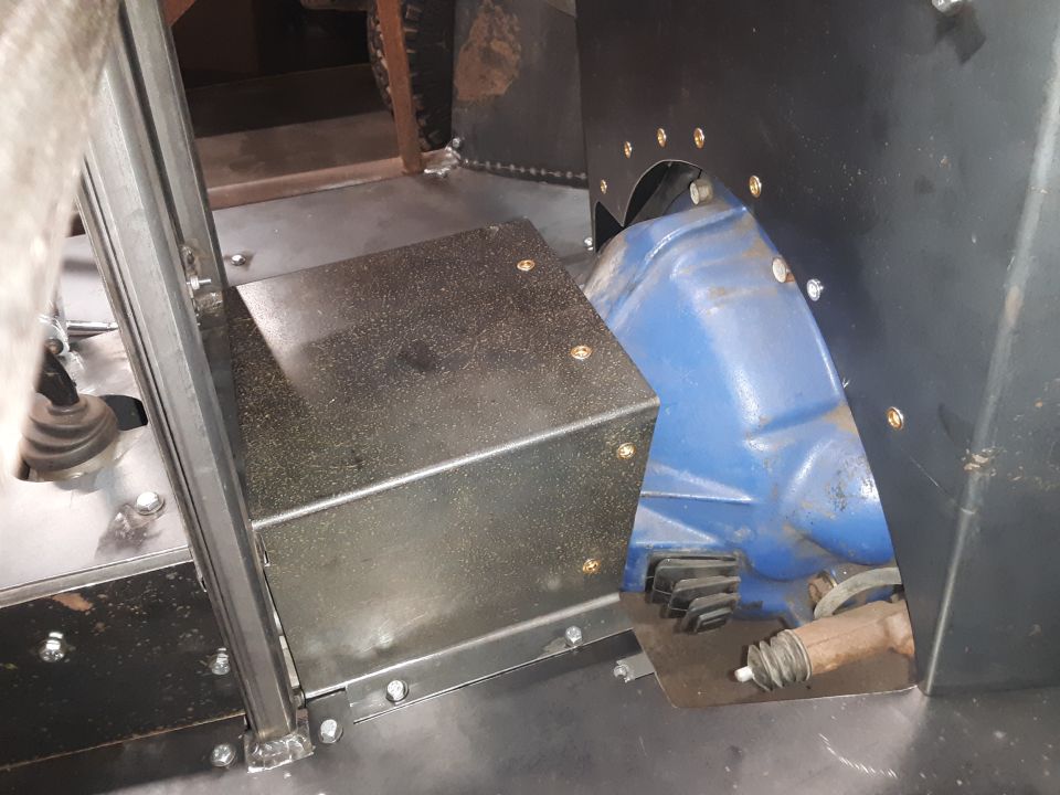 Close-up of a vehicle's transmission tunnel with a blue transmission housing and a black metal cover
