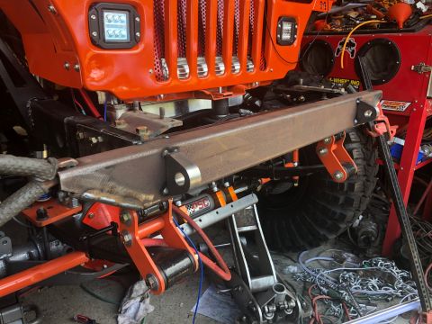1992 Jeep Wrangler - The front end of an orange Jeep Wrangler is shown with a custom bumper and suspension components during a repair or modification.