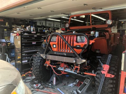 1992 Jeep Wrangler - This orange 1990 Jeep Wrangler is in a garage, possibly undergoing modifications, with its front end visible.