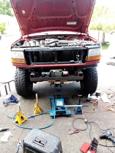 1994 Ford Bronco - A red Ford truck is being worked on, with its hood up and front end elevated by jacks.