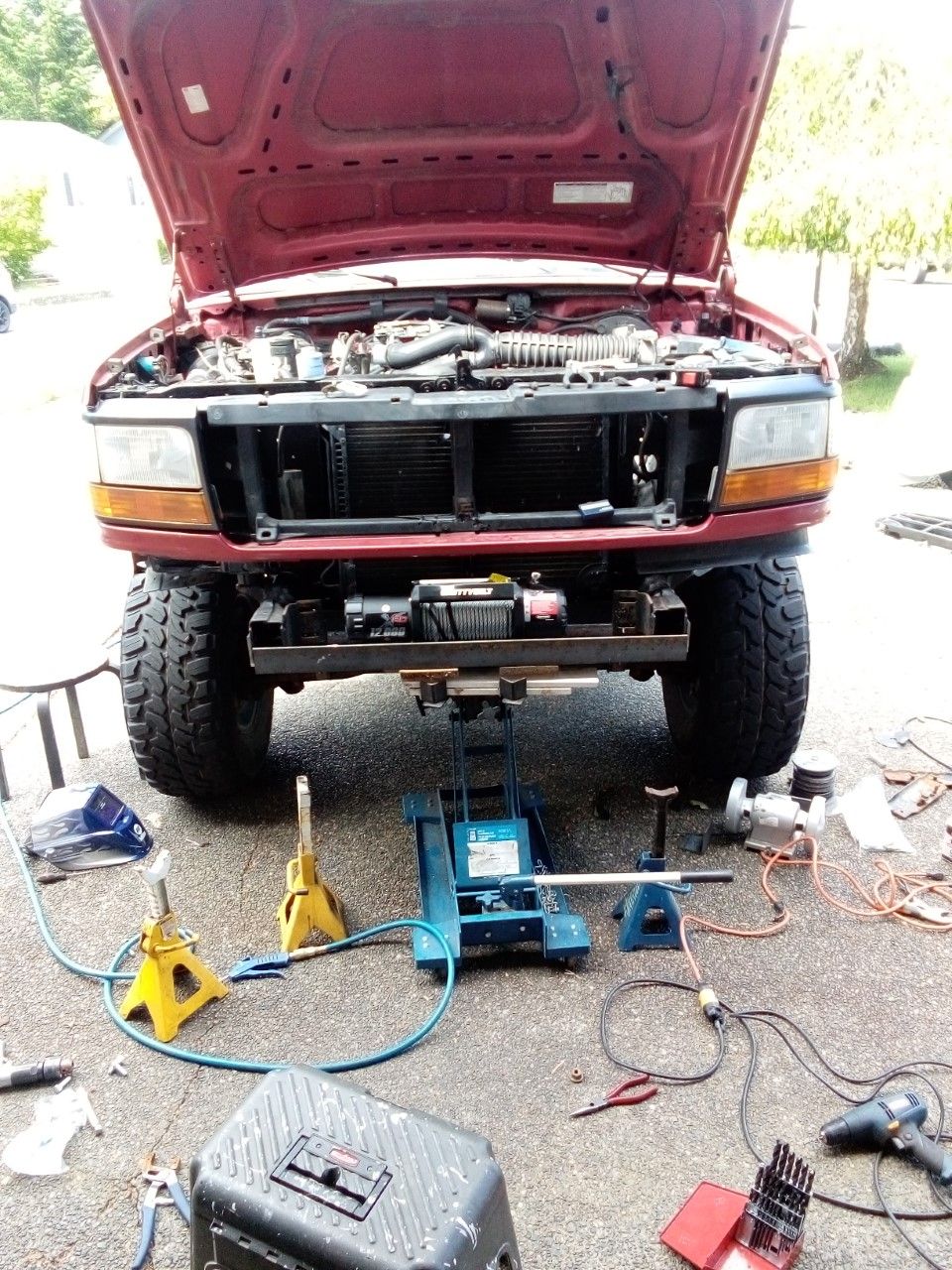 Red Ford truck with hood open, front view, jacked up, with winch installed on custom bumper