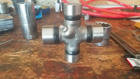 1985 Ford Bronco - Close-up of a universal joint, a critical component for transferring rotational power, resting on a wooden surface.