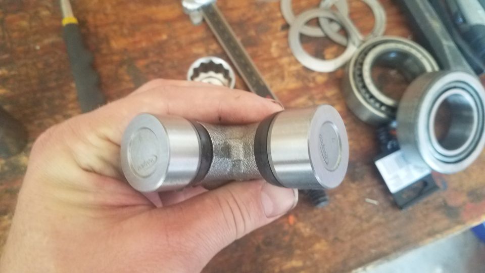 Hand holding a universal joint with bearings and tools in the background
