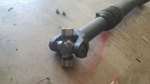 1985 Ford Bronco - A driveshaft universal joint lies on a concrete surface next to two small nuts.