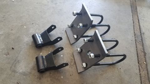 1985 Ford Bronco - Set of aftermarket leaf spring shackles and U-bolts, likely for suspension modification, laid out on a concrete surface.