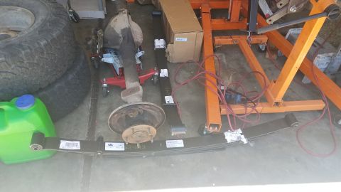 1985 Ford Bronco - Vehicle axle and leaf springs are shown on the ground, possibly for repair or replacement.