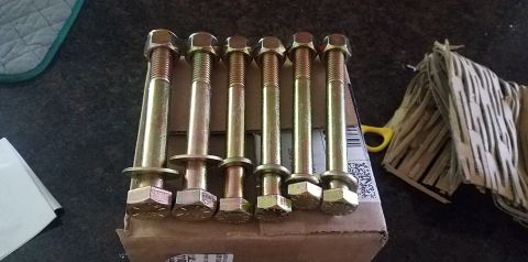 1985 Ford Bronco - A set of six bolts with nuts and washers are laid out on a cardboard box, with some packing material visible to the right.