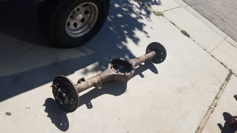 1985 Ford Bronco - A rear axle assembly is shown on a concrete surface, with a vehicle tire visible in the upper left corner.