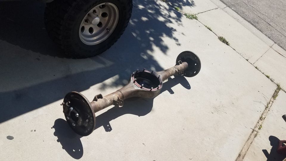 Rear axle assembly with brake drums removed, resting on concrete next to a tire