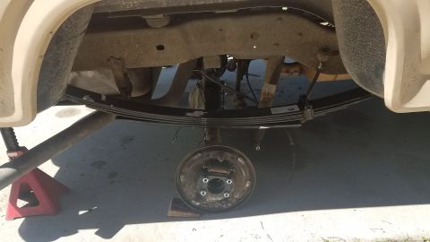 1985 Ford Bronco - The rear suspension components of a vehicle are visible, with the brake drum removed and leaf springs exposed.