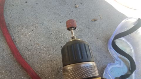 1985 Ford Bronco - Tools for automotive work, including a drill with a sanding attachment and safety glasses, rest on a concrete surface.