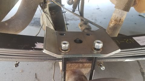 1985 Ford Bronco - A metal plate is bolted onto the leaf spring assembly of a vehicle, likely for suspension modification.