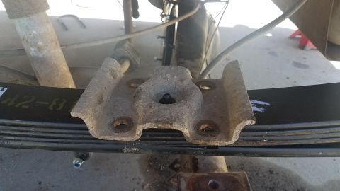 1985 Ford Bronco - Vehicle suspension part: a rusty bracket attached to a leaf spring with visible markings.