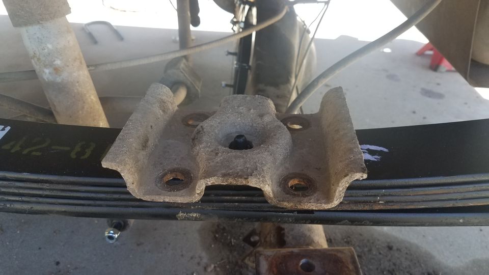 Close-up of a rusty leaf spring bracket on a vehicle's suspension. Black leaf spring has yellow markings '42-8'