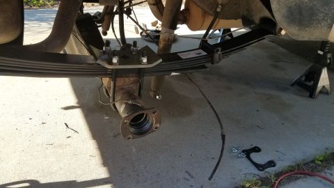 1985 Ford Bronco - The rear axle assembly of a vehicle, supported by jack stands, shows leaf springs and U-bolts.