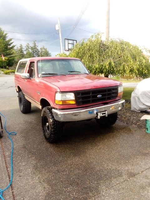 1994 Ford Bronco - A red Ford Bronco with a white top is parked on a wet asphalt driveway.
