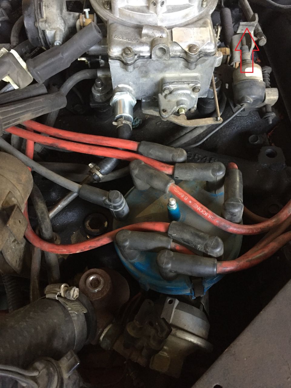 Close-up of a V8 engine's carburetor, distributor cap, and red spark plug wires