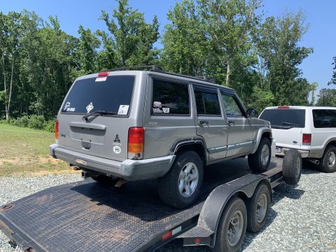 2000 Jeep Cherokee - A silver Jeep Cherokee is being transported on a trailer, with another SUV visible behind it.