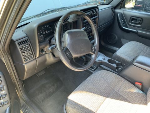 2000 Jeep Cherokee - The interior of a Jeep Cherokee shows gray patterned seats and a dark gray dashboard with the Jeep logo on the steering wheel.