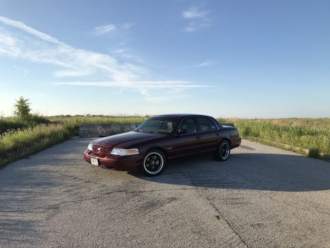 2004 Ford Crown Victoria - A maroon Ford Crown Victoria is parked on a paved surface under a partly cloudy sky.