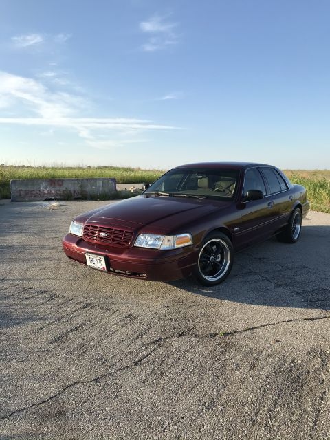 2004 Ford Crown Victoria - A maroon Ford Crown Victoria is parked on a cracked asphalt surface under a clear blue sky.