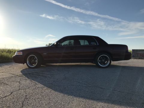 2004 Ford Crown Victoria - A dark red 2004 Ford Crown Victoria is shown from the side under a partly cloudy sky.