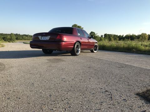 2004 Ford Crown Victoria - Rear view of a red 2004 Ford Crown Victoria with custom wheels parked on a road.