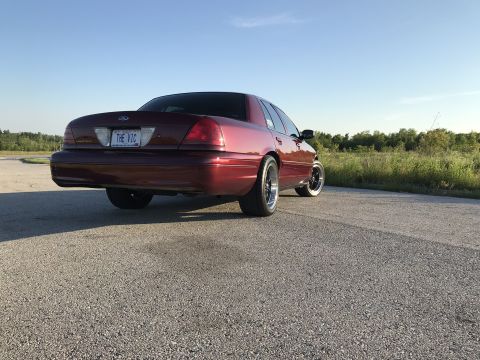 2004 Ford Crown Victoria - A red Ford Crown Victoria is shown from the rear on a paved road with a clear blue sky above.