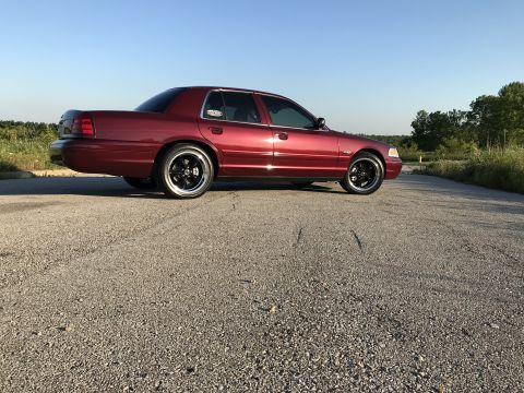 2004 Ford Crown Victoria - A red 2004 Ford Crown Victoria is parked on a gravel road with trees in the background.