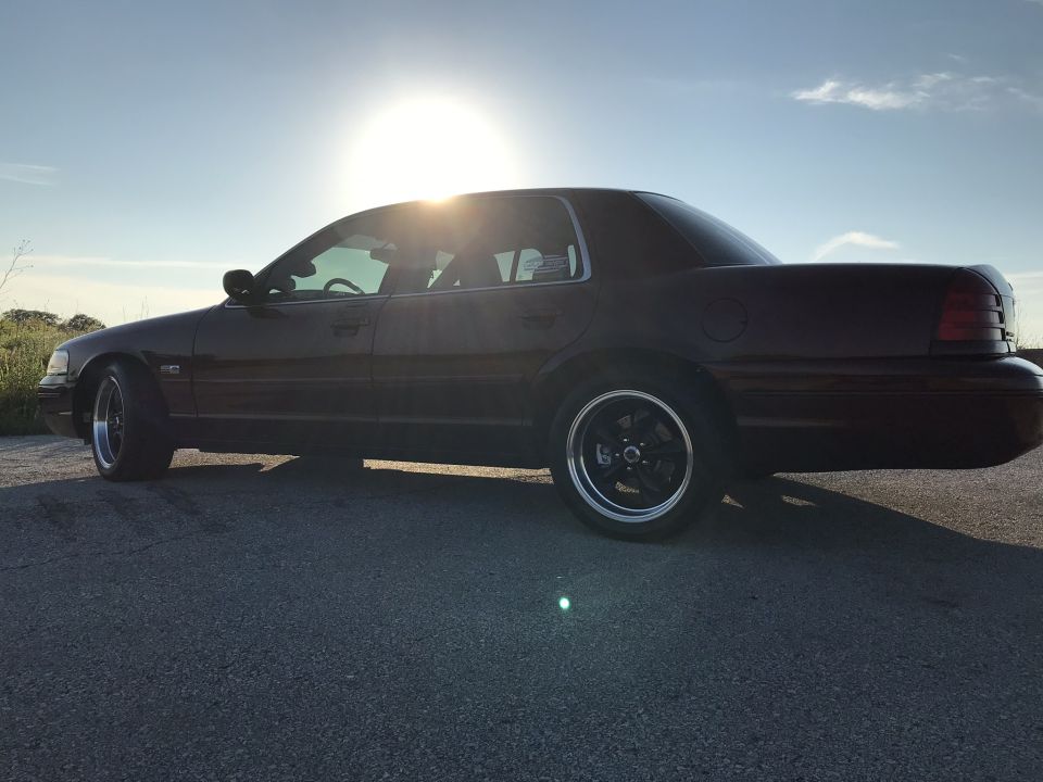 Dark red 2004 Ford Crown Victoria sedan with aftermarket wheels, seen from the side at sunset