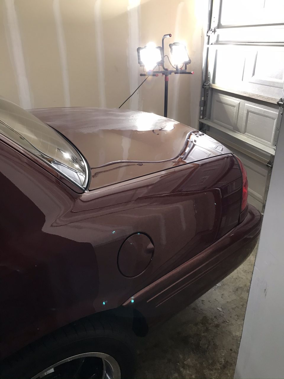 maroon sedan's trunk and rear quarter panel in a garage, with a fuel door visible