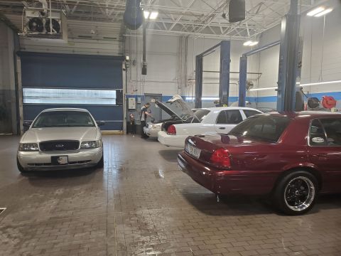 2004 Ford Crown Victoria - Three Ford Crown Victorias are parked in a garage, two of them are white and one is maroon.