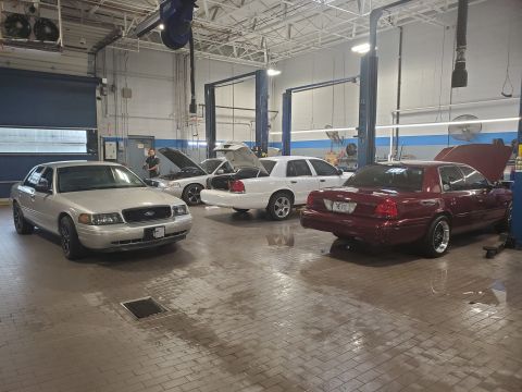 2004 Ford Crown Victoria - Three Ford Crown Victorias are parked in a service bay, with two having their hoods open.