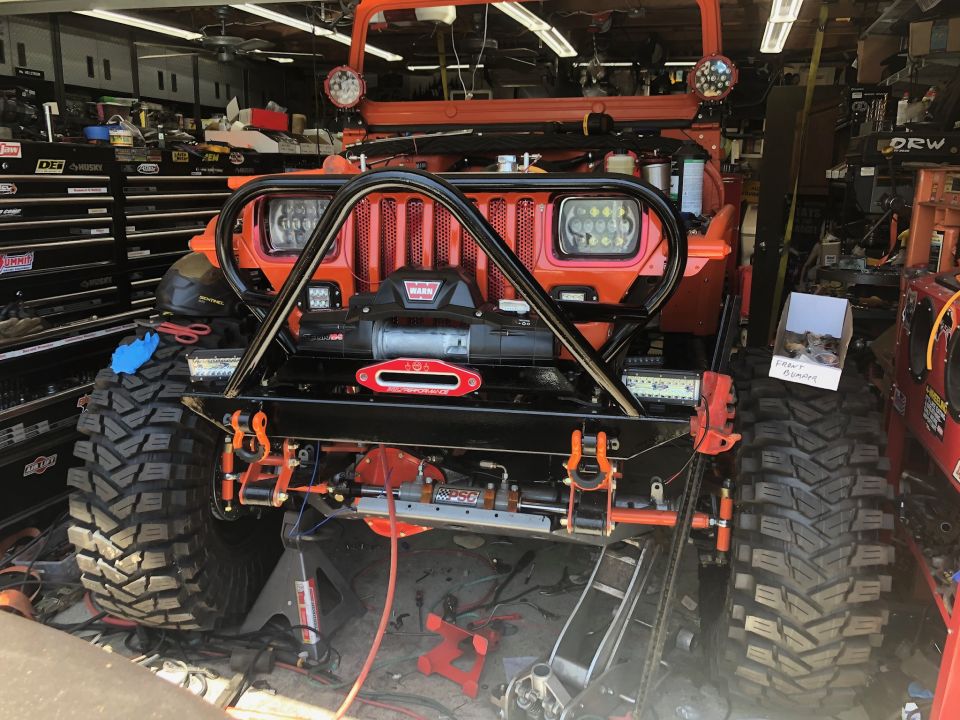 Orange Jeep Wrangler with winch, custom bumper, and large off-road tires, parked in a garage