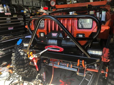 1992 Jeep Wrangler - Front view of an orange Jeep Wrangler with aftermarket winch and roll cage, parked in a workshop.