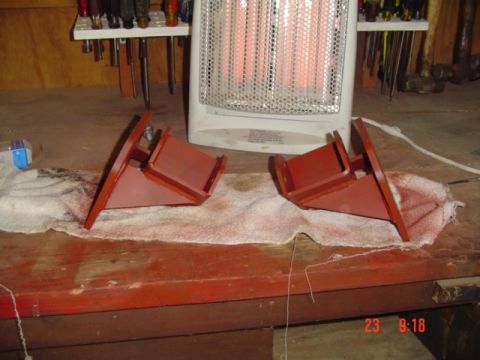 1989 Ford Bronco - Two red metal brackets are placed on a cloth on a workbench, with a heater and tools visible.