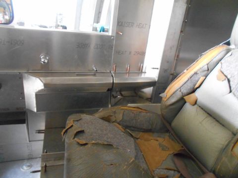 1992 Ford Bronco - The interior of a vehicle shows heavily worn and torn seats next to metal paneling with heat-related markings.