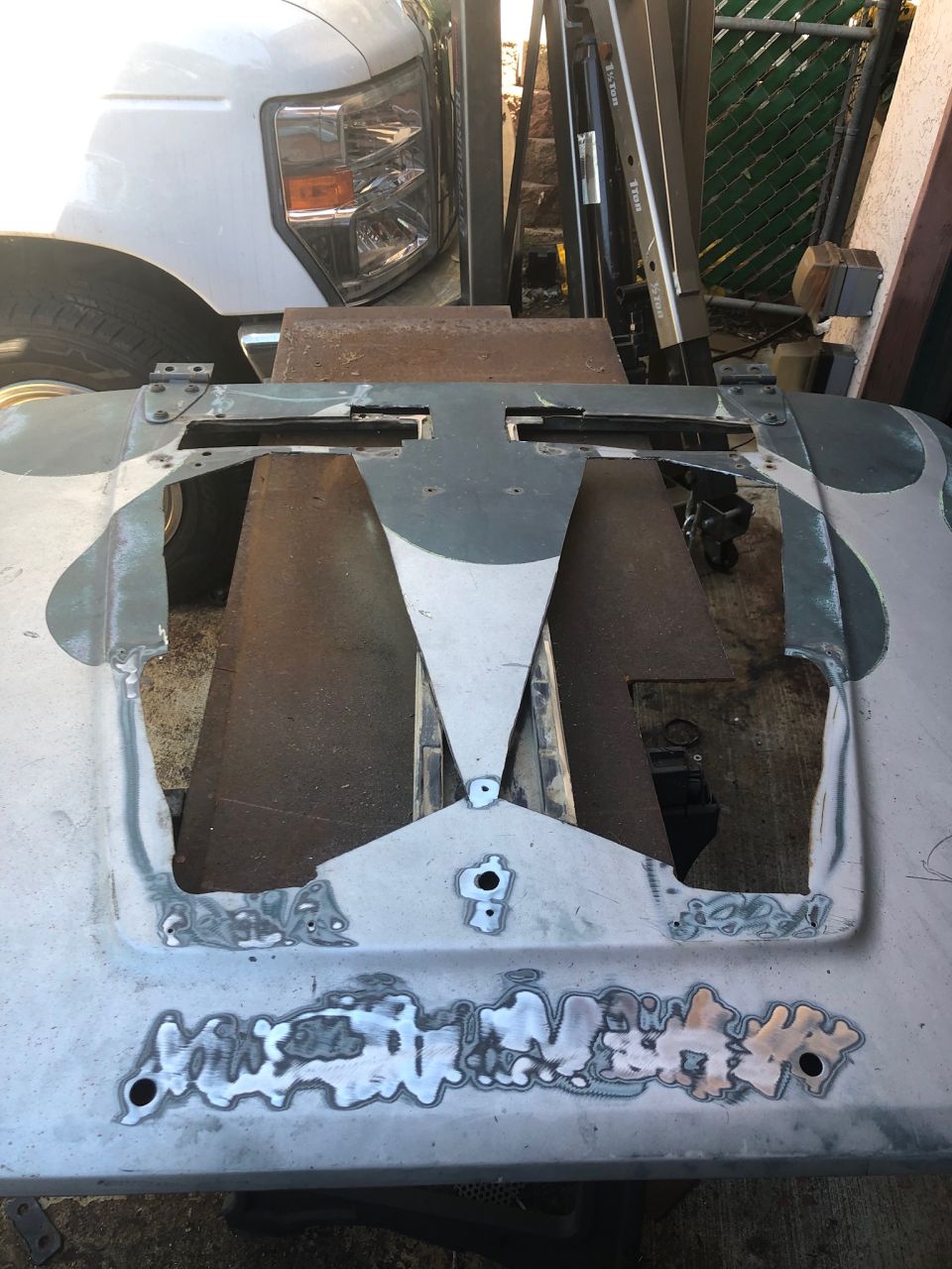 Car hood with welded patches and cutouts, showing metalwork