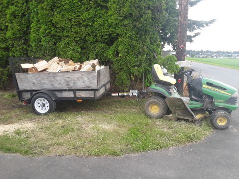 1985 Toyota Hilux - A green John Deere LA145 riding mower is hitched to a utility trailer filled with cut firewood.