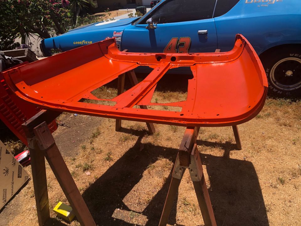 Orange car hood on sawhorses, blue Dodge Charger in background